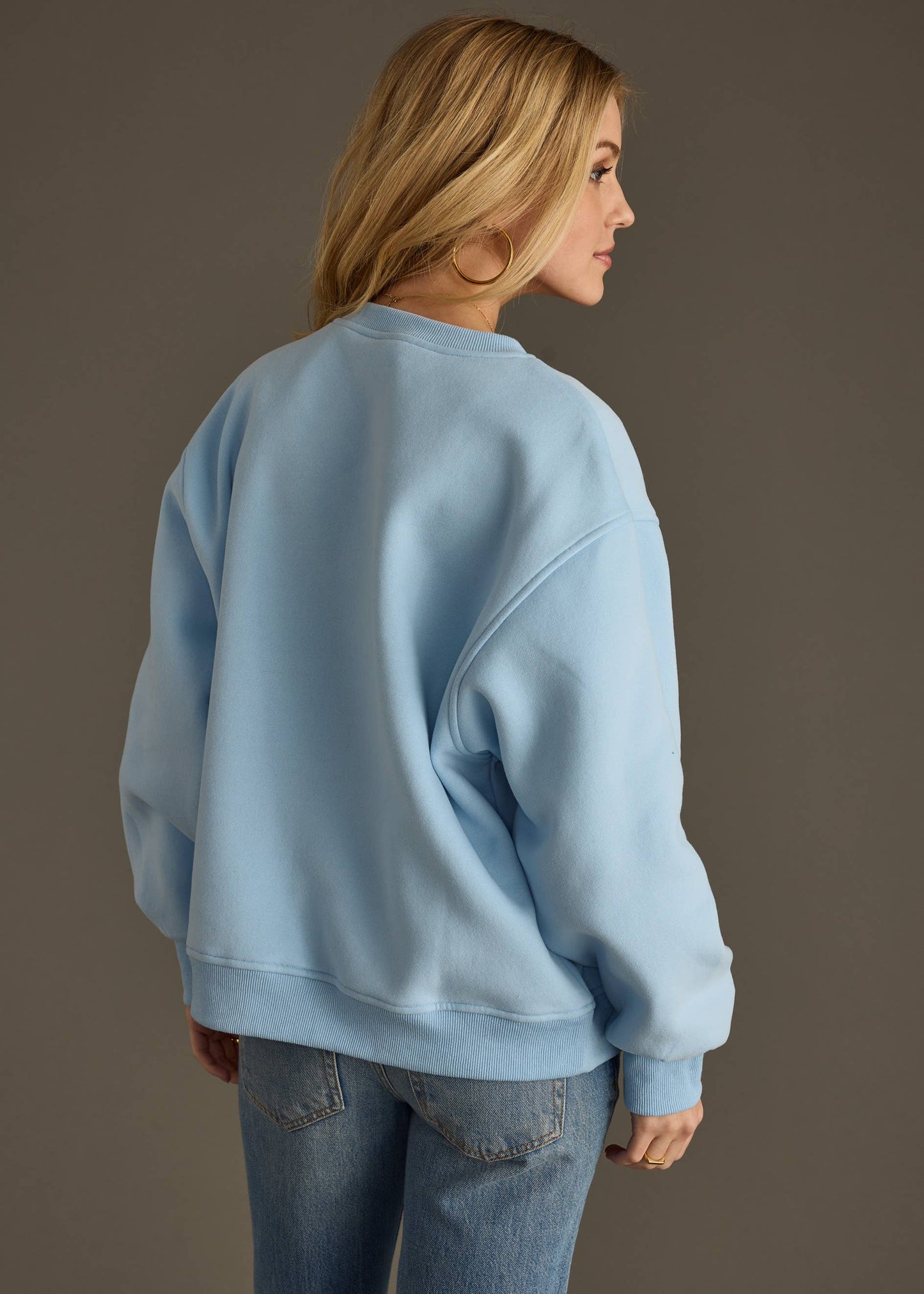 Woman wearing a light blue sweatshirt with colorful 'ADVENTURE' text on a plain background