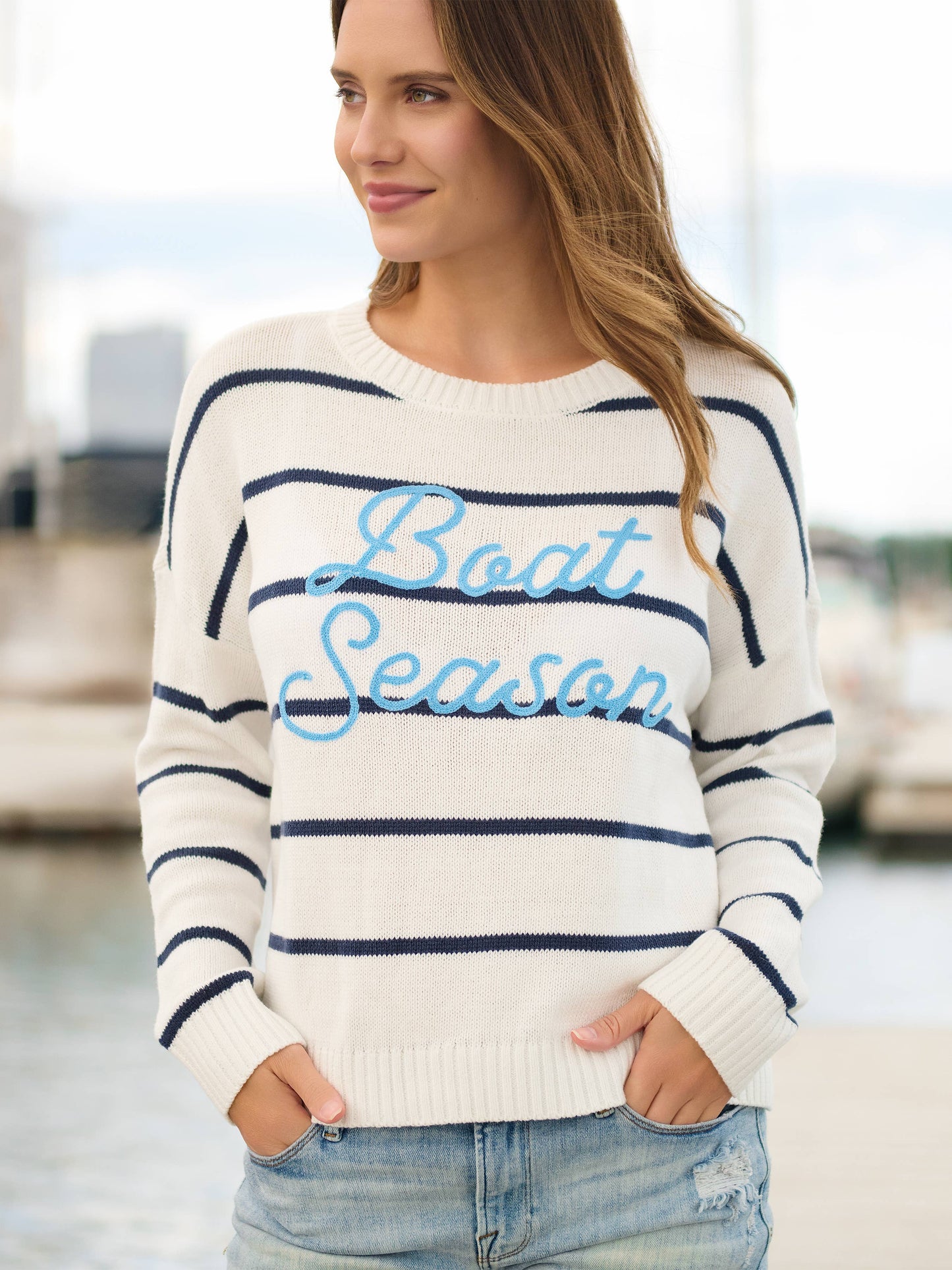Woman wearing a striped sweater with 'Boat Season' text by a waterfront.