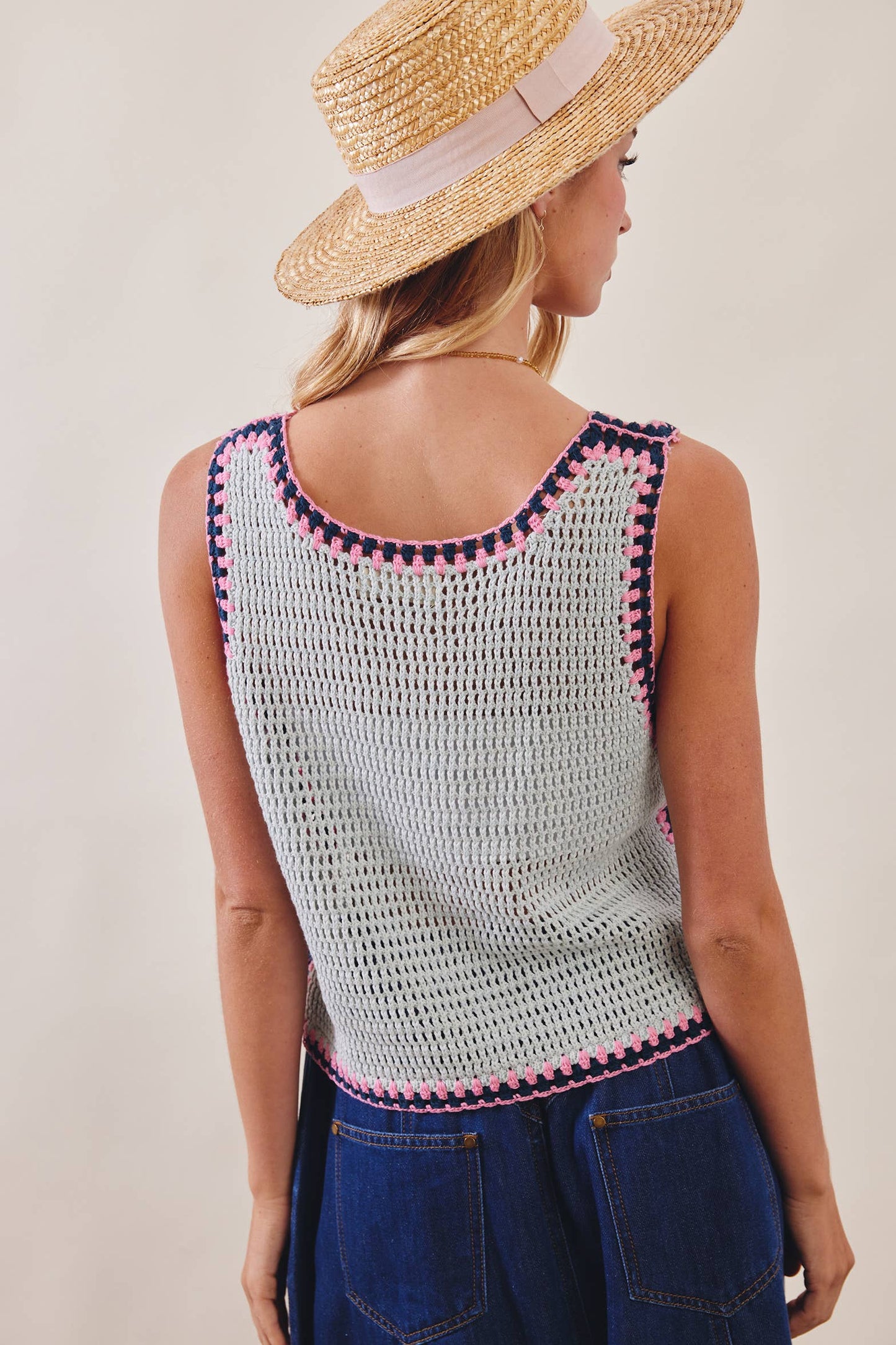 Woman wearing a crochet top with pink trim and a straw hat on a plain background