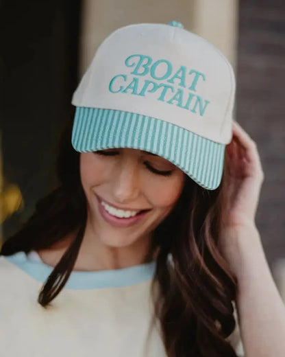 Woman wearing a cap with 'BOAT CAPTAIN' text, smiling outdoors.