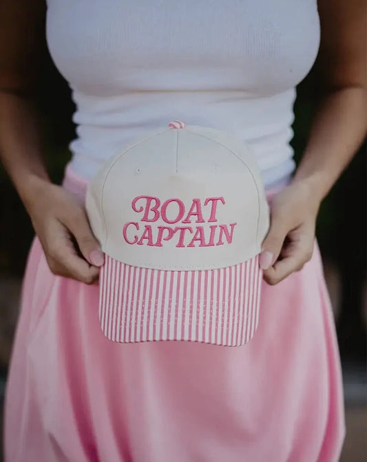Person holding a cap with 'BOAT CAPTAIN' text in a casual setting