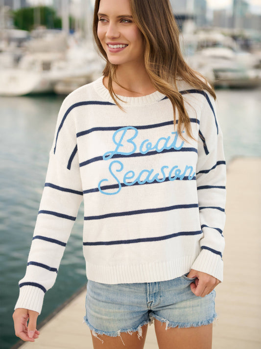 Woman wearing a striped sweater with 'Boat Season' text by a marina.