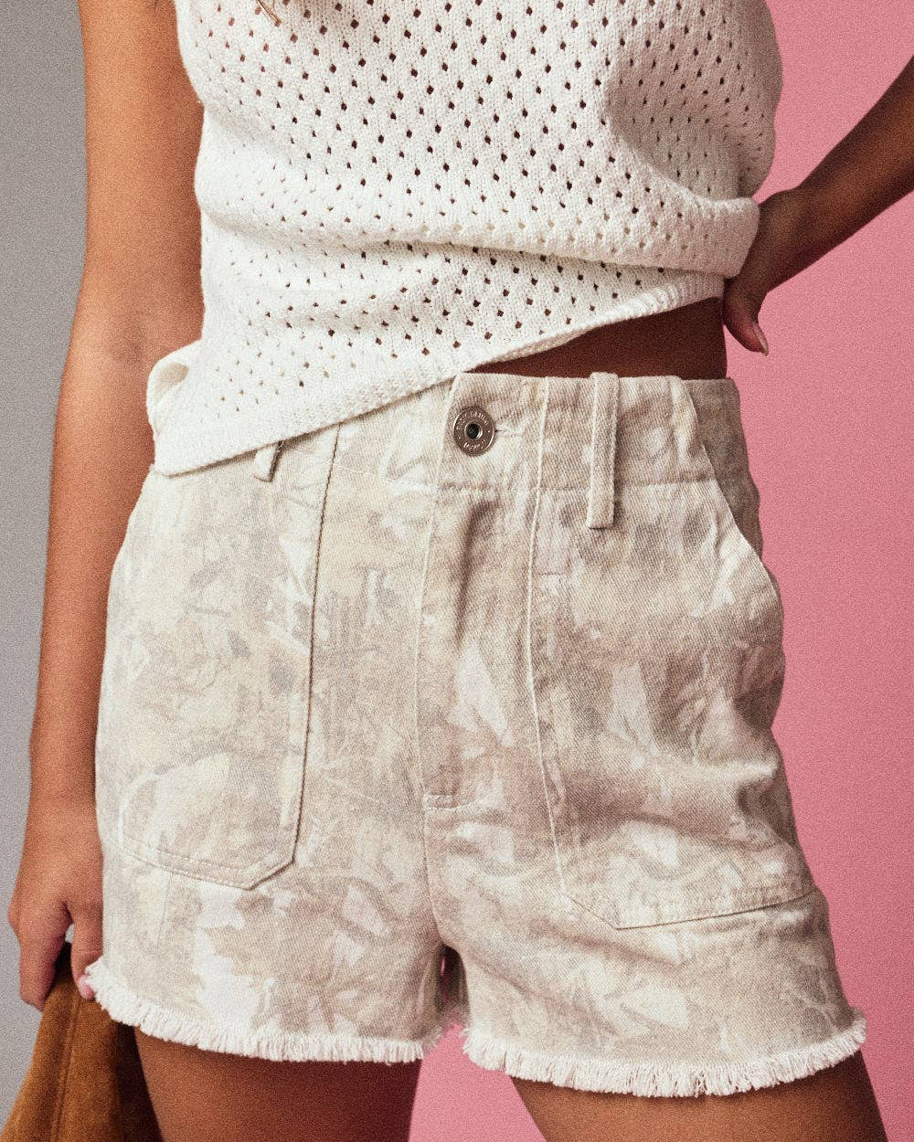 Person wearing a white sleeveless top and beige shorts against a pink background