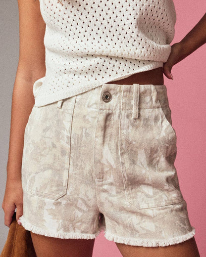 Person wearing a white sleeveless top and beige shorts against a pink background