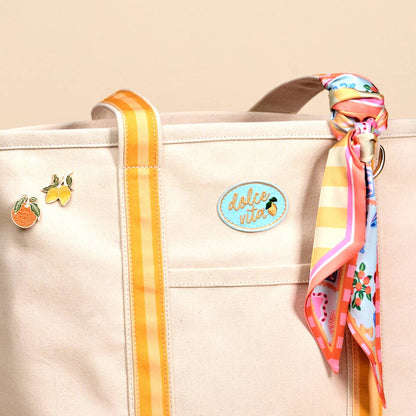 Beige tote bag with colorful ribbon, earrings, and decorative tag on a beige background