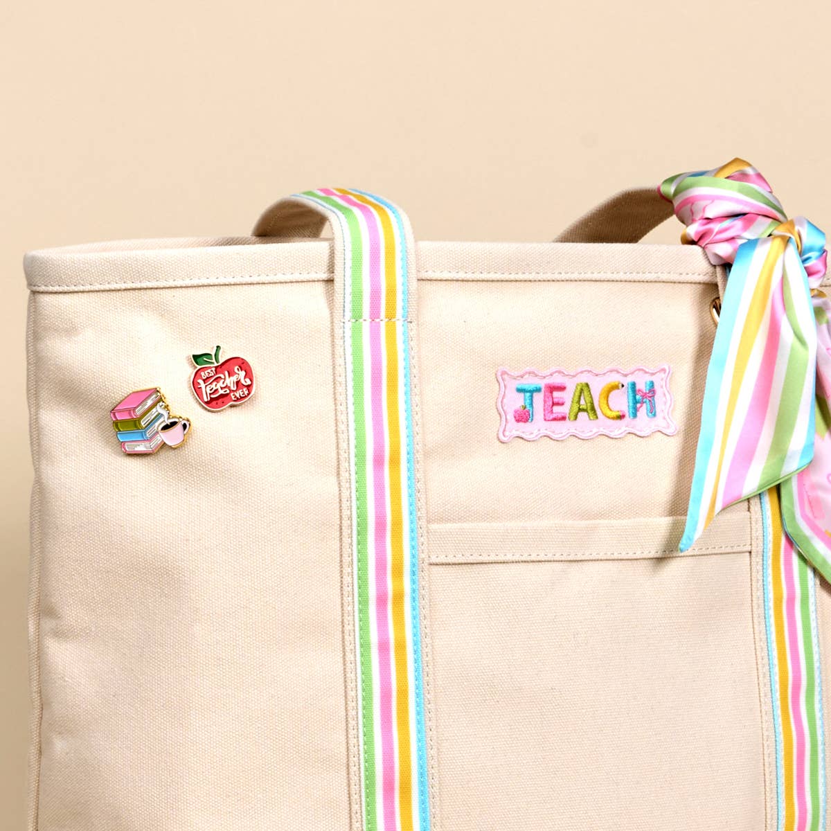 Beige tote bag with colorful ribbons and 'TEACH' patch on a beige background