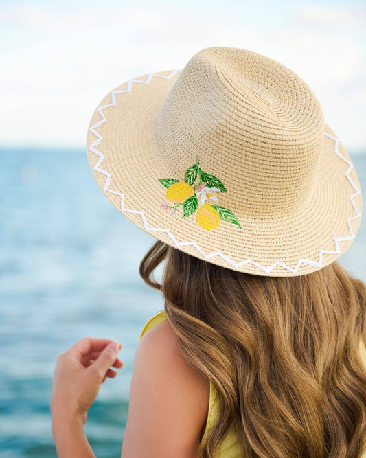 Person wearing a straw hat with lemon designs by the ocean