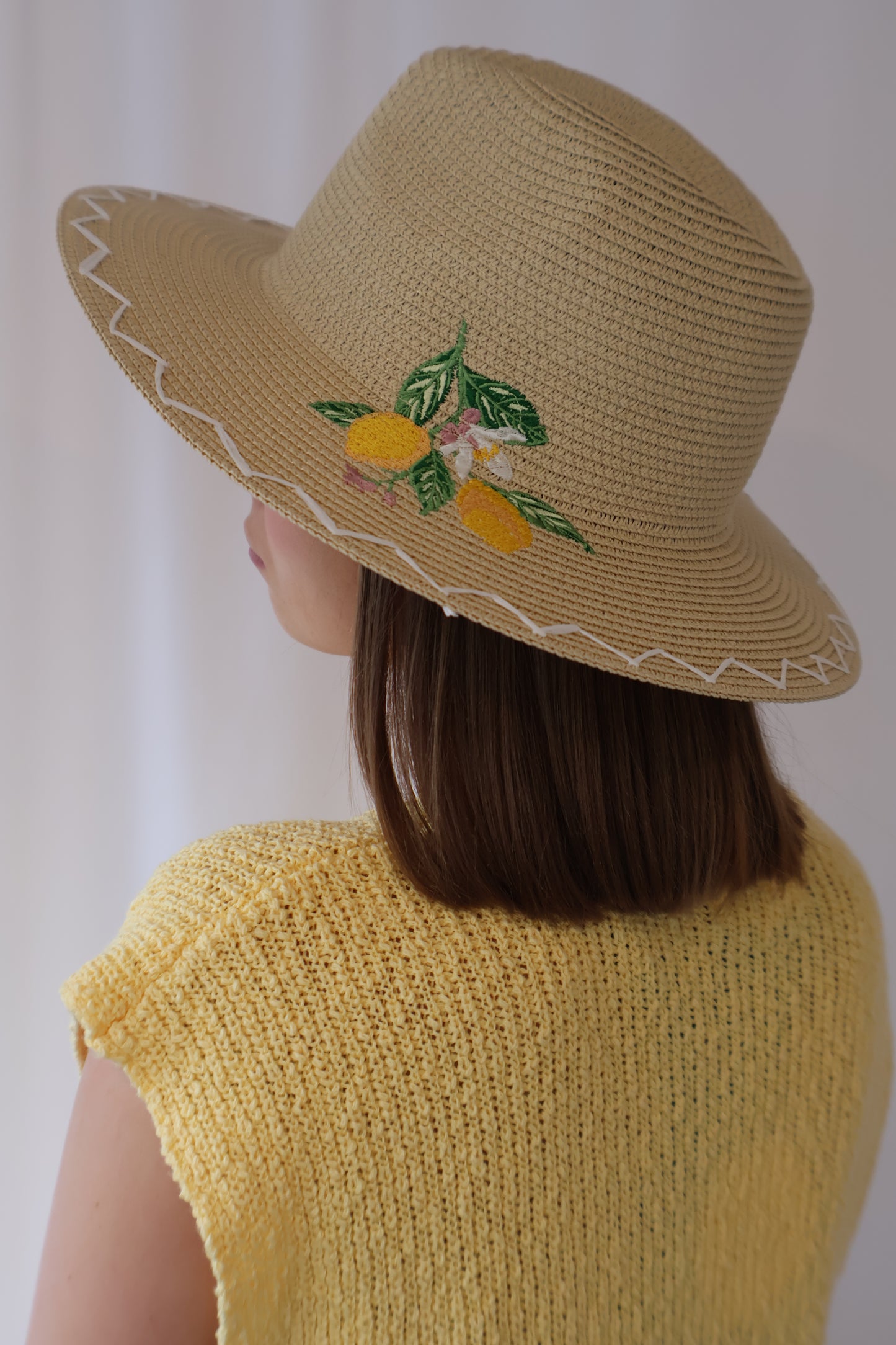 Person wearing a yellow knit top and straw hat with lemon design on a white background