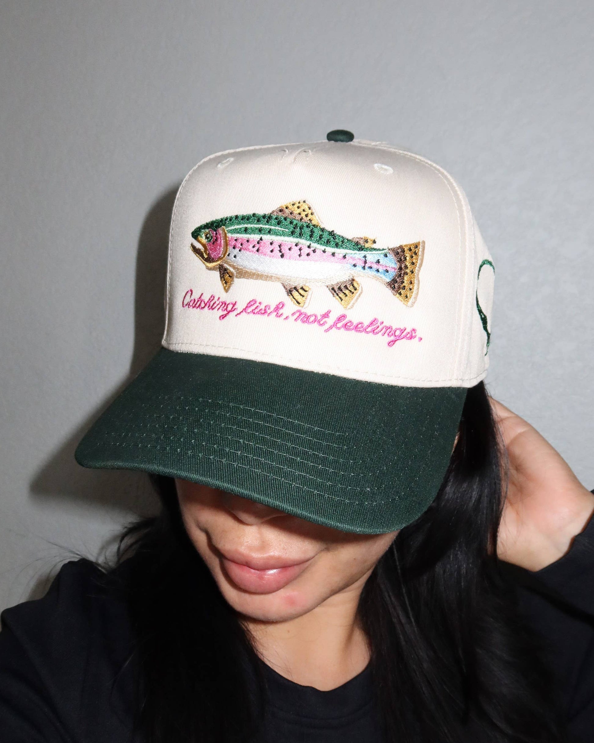 Person wearing a cap with a fish design and text on a plain background