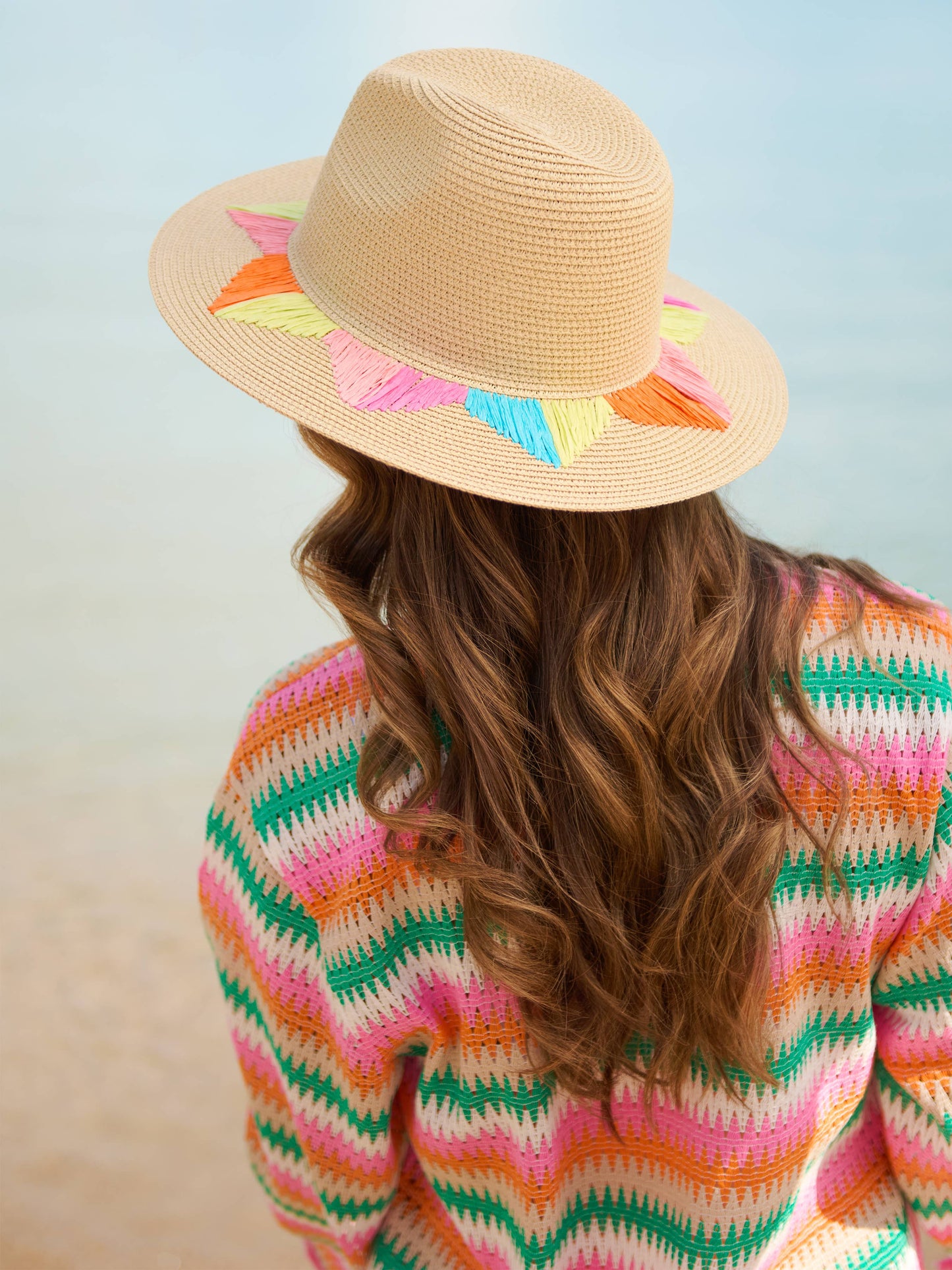 Person wearing a colorful straw hat with rainbow accents and a multicolored sweater.