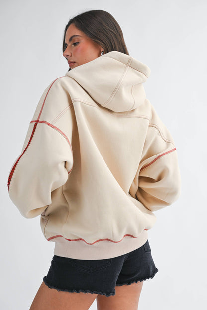 Woman wearing a beige hoodie with red accents on a white background