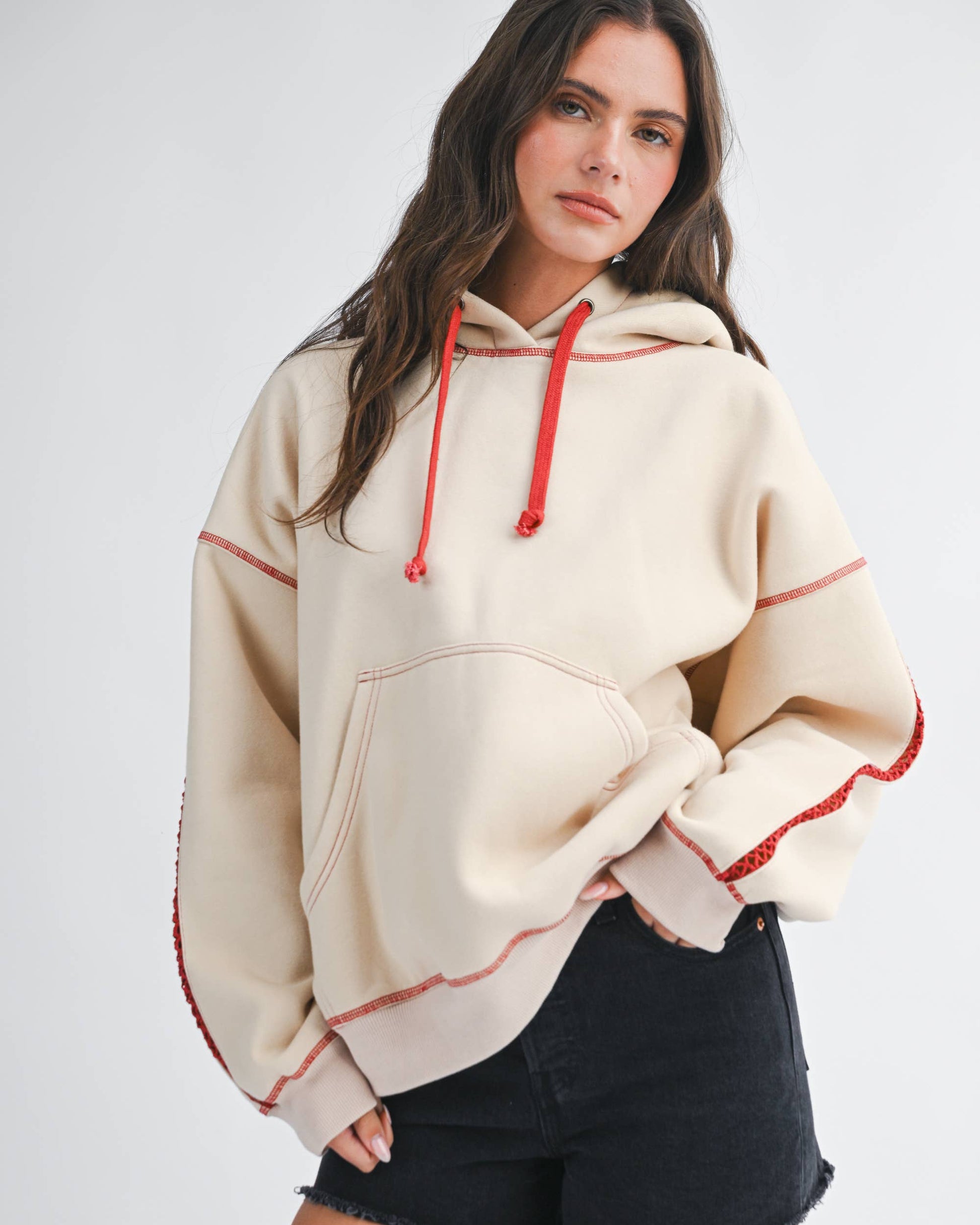 Woman wearing a beige hoodie with red accents and black shorts on a white background