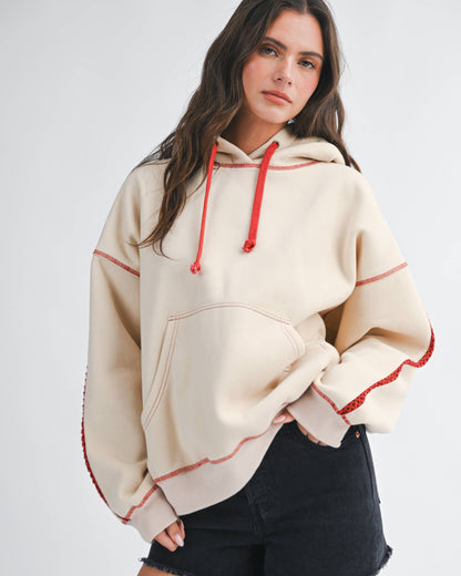 Woman wearing a beige hoodie with red accents and black shorts on a white background