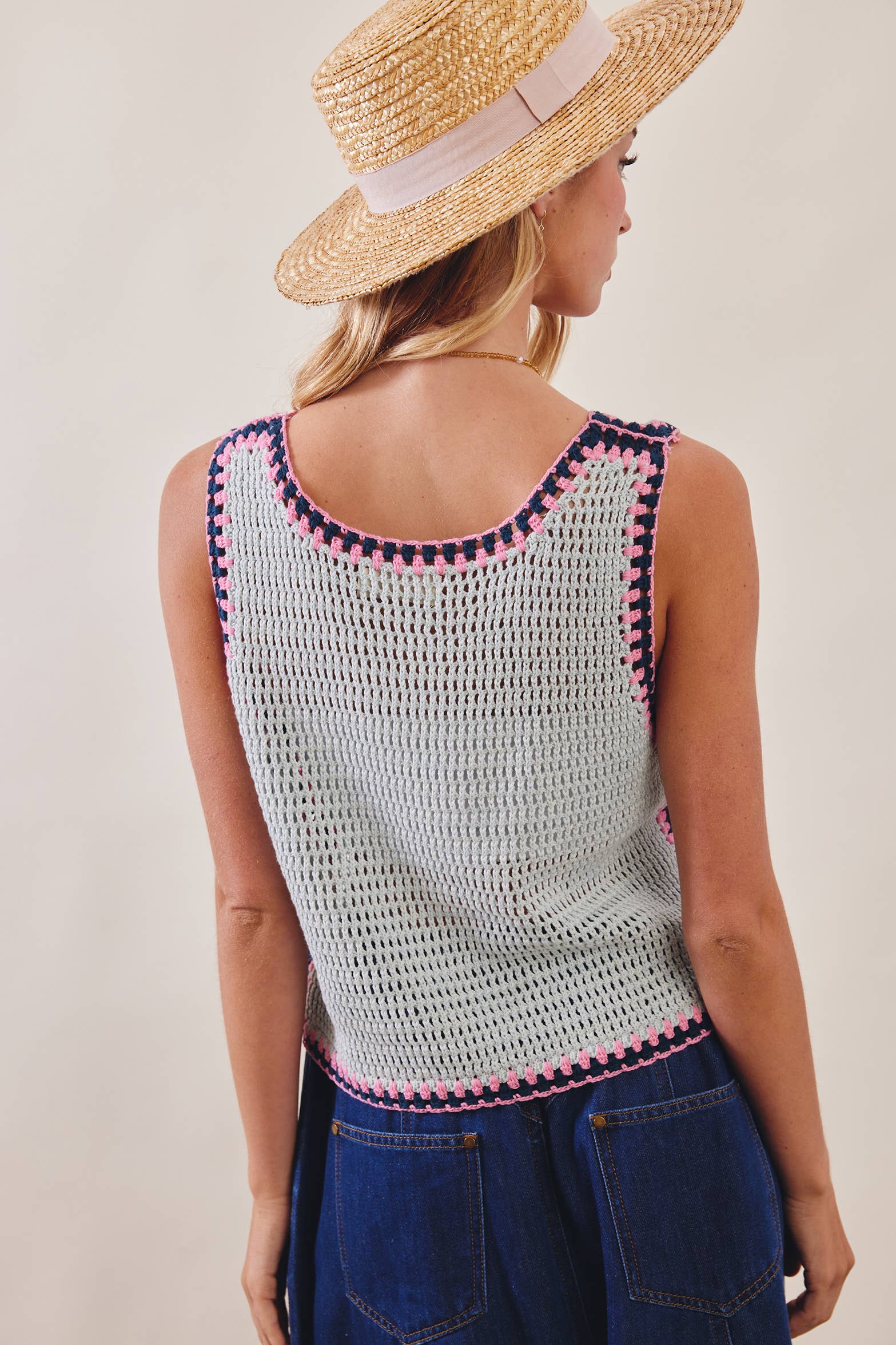 Woman wearing a crochet top with pink trim and a straw hat on a plain background