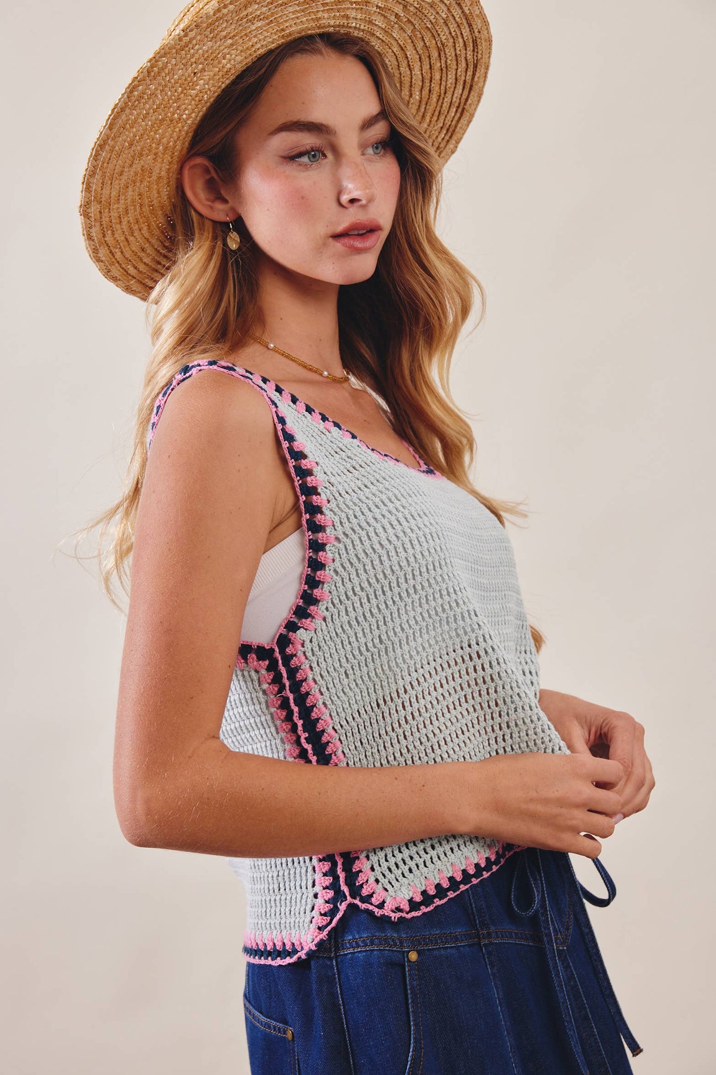 Woman wearing a crochet top with pink trim and a straw hat on a plain background