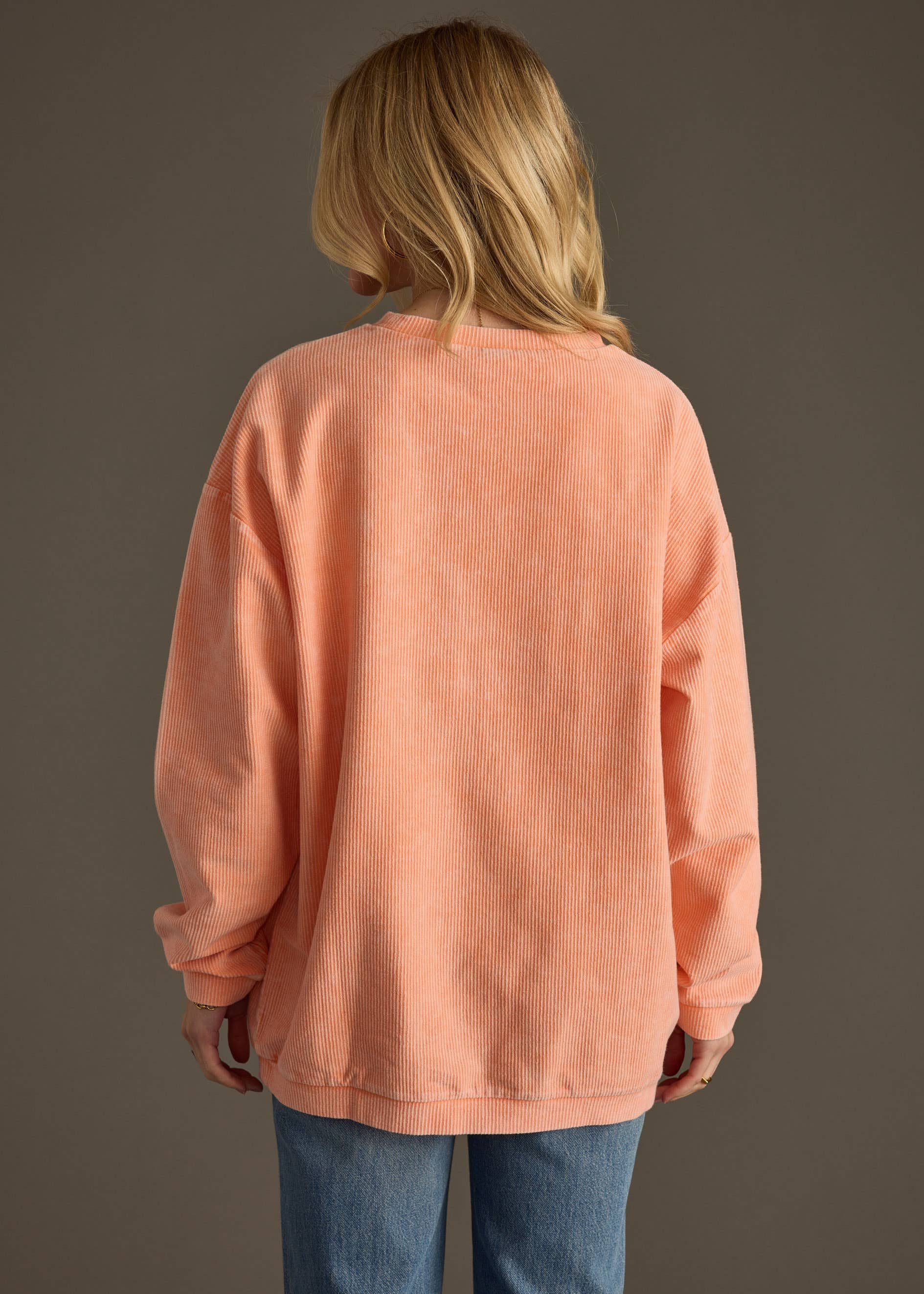 Woman wearing a peach sweatshirt with 'DAY DRINKING' text on a gray background