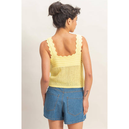 Woman wearing a yellow crochet top and blue denim shorts on a plain background
