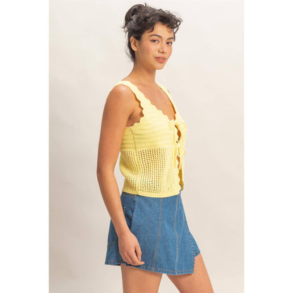 Woman wearing a yellow sleeveless top and blue denim skirt on a plain background