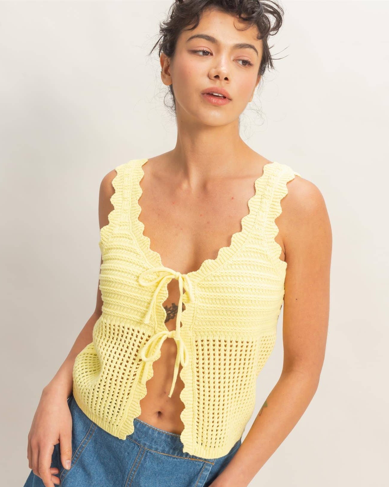 Woman wearing a yellow crochet top and denim shorts on a plain background