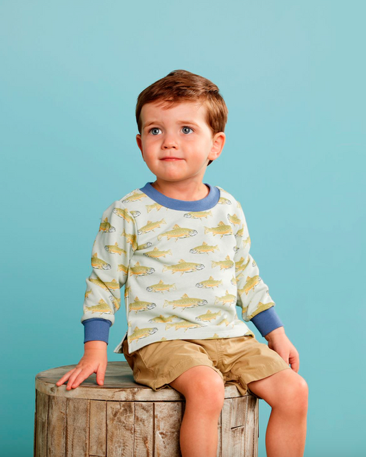 Young boy wearing a shirt with fish pattern sitting on a wooden block against a blue background