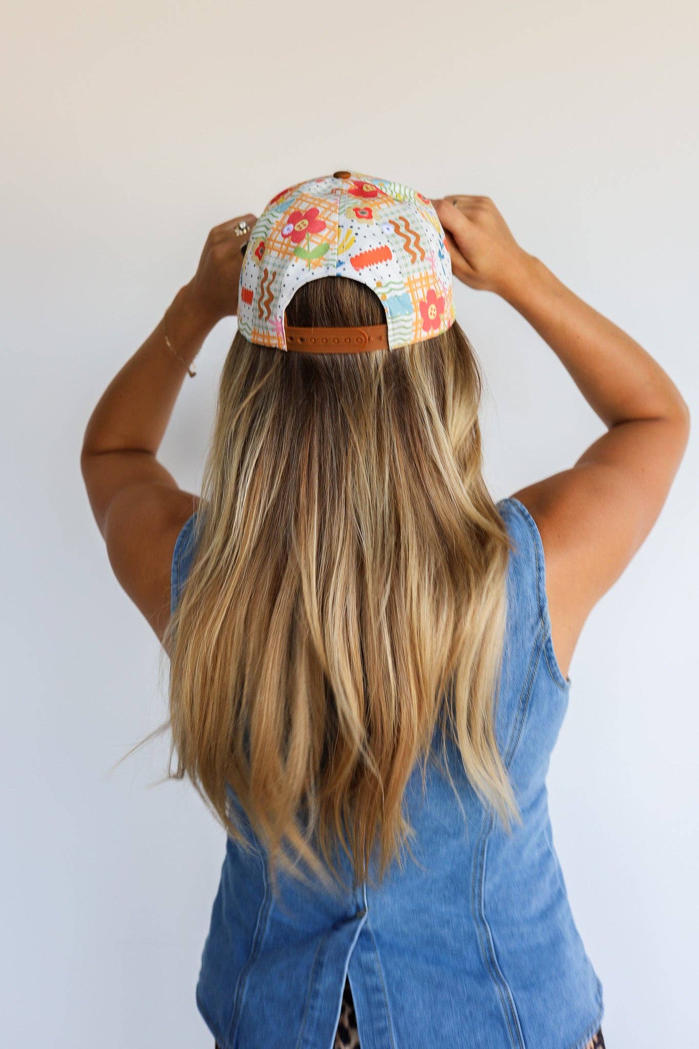 Person wearing a colorful floral cap with their back to the camera on a white background
