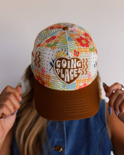 Colorful cap with 'Going Places' text held by a person wearing a denim jacket.