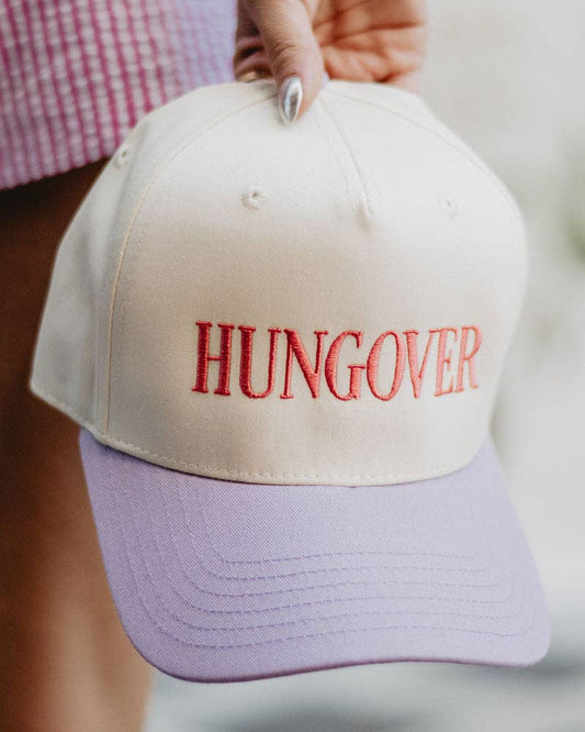 Beige cap with 'HUNGOVER' in red text held by a person wearing a checkered shirt.