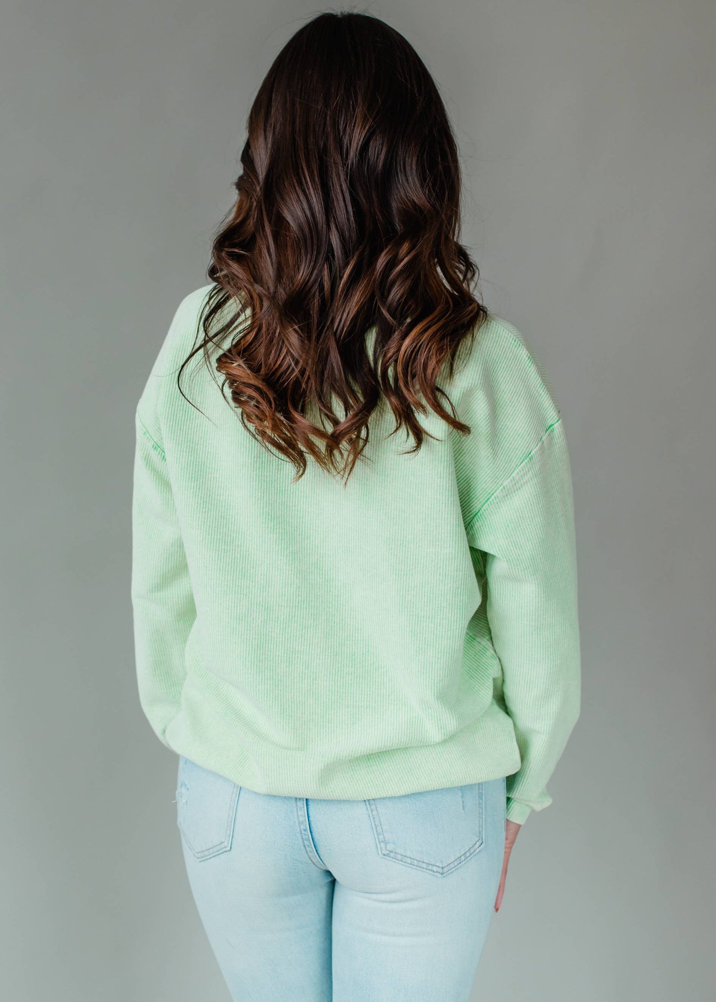Woman wearing a light green sweatshirt with text, standing against a plain background