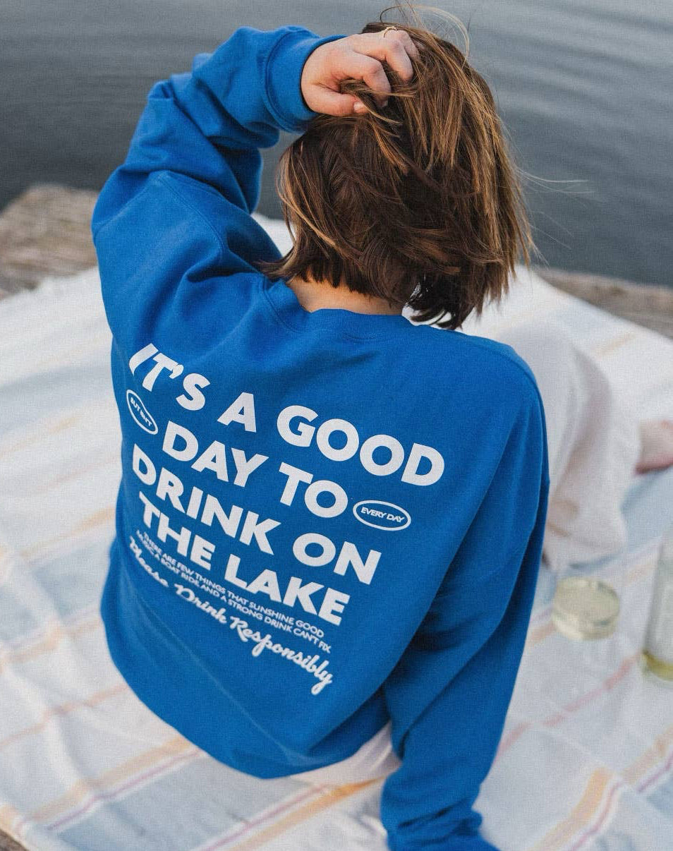 Person wearing a blue sweatshirt with text by a lake