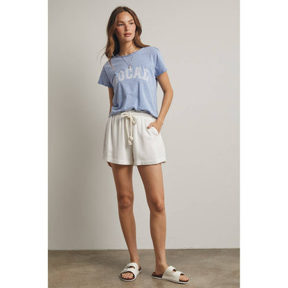 Woman wearing a blue t-shirt and white shorts against a plain background
