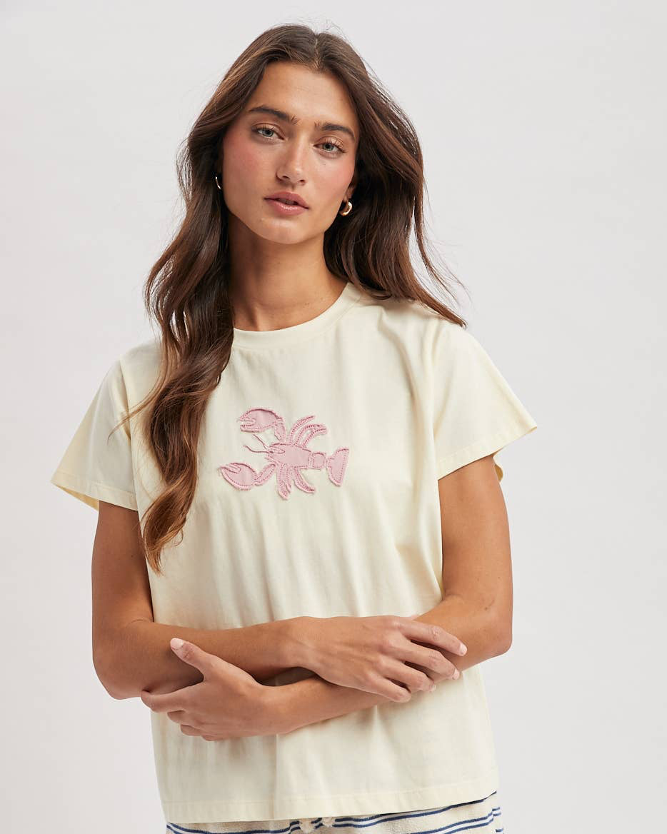 Woman wearing a cream t-shirt with a pink lobster design and striped shorts on a white background