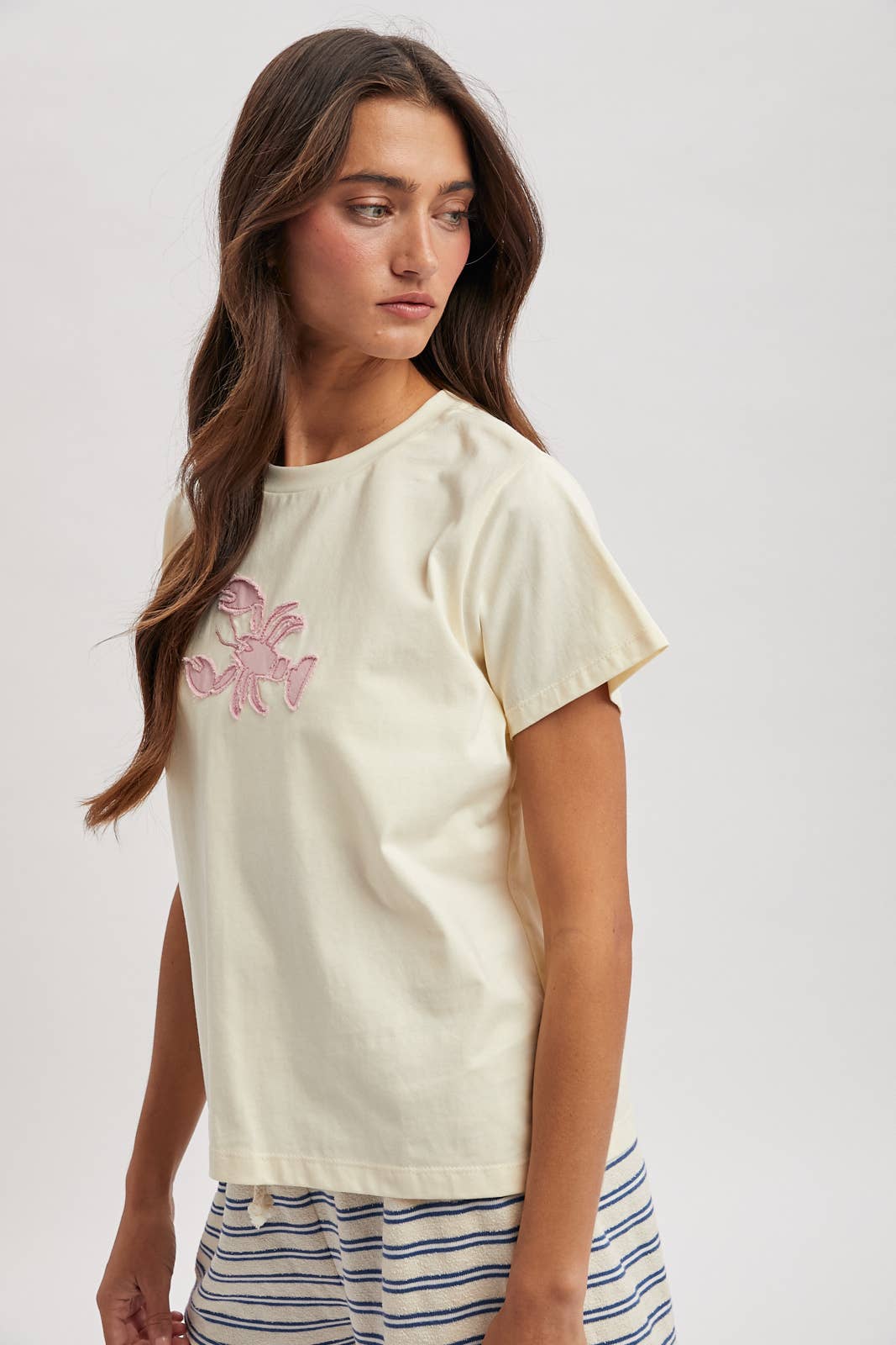 Woman wearing a cream t-shirt with a pink floral design on a plain background