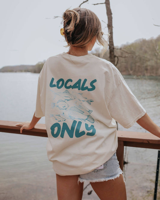 Person wearing a 'Locals Only' shirt by a lake