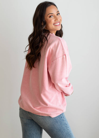 Woman wearing a pink sweatshirt with 'margs.' text on a plain background