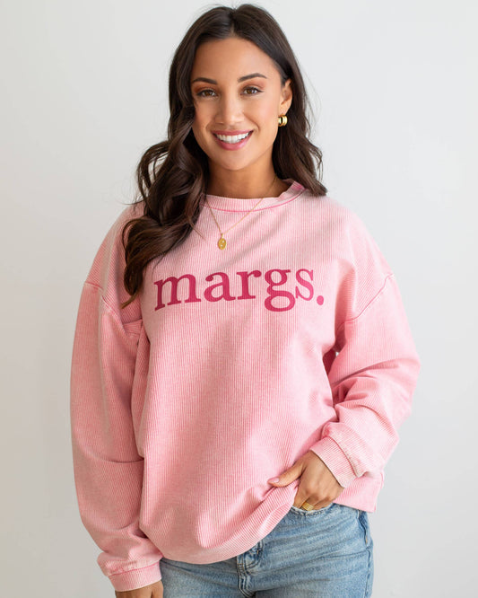Woman wearing a pink sweatshirt with 'margs.' text on a plain background