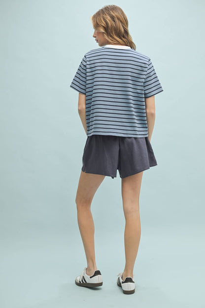 A woman wearing a striped knit top with the text 'MEET ME AT THE LAKE' on it, in a color palette that includes blue and white tones.