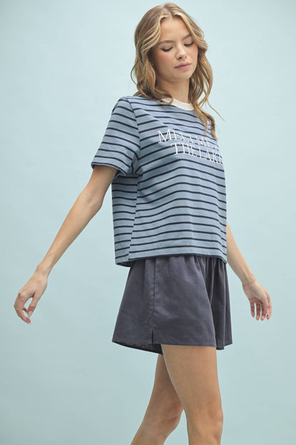 A woman wearing a striped knit top with the text 'MEET ME AT THE LAKE' on it, in a color palette that includes blue and white tones.