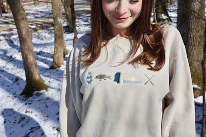Person wearing a light-colored sweatshirt with lake graphic designs outdoors in a snowy forest.
