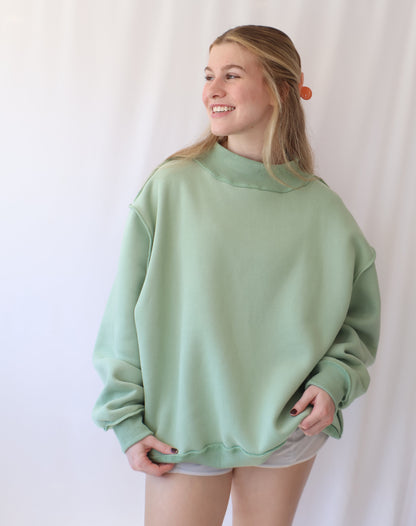 Person wearing a light green sweatshirt and white shorts on a plain background