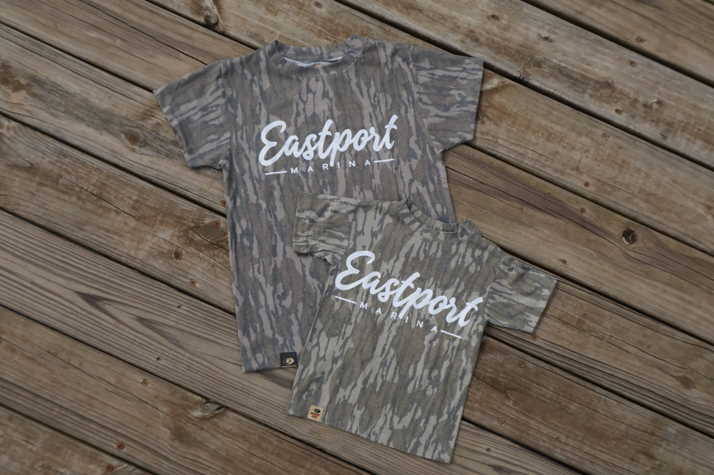 Two camouflage-patterned shirts with 'Eastport' branding on a wooden surface