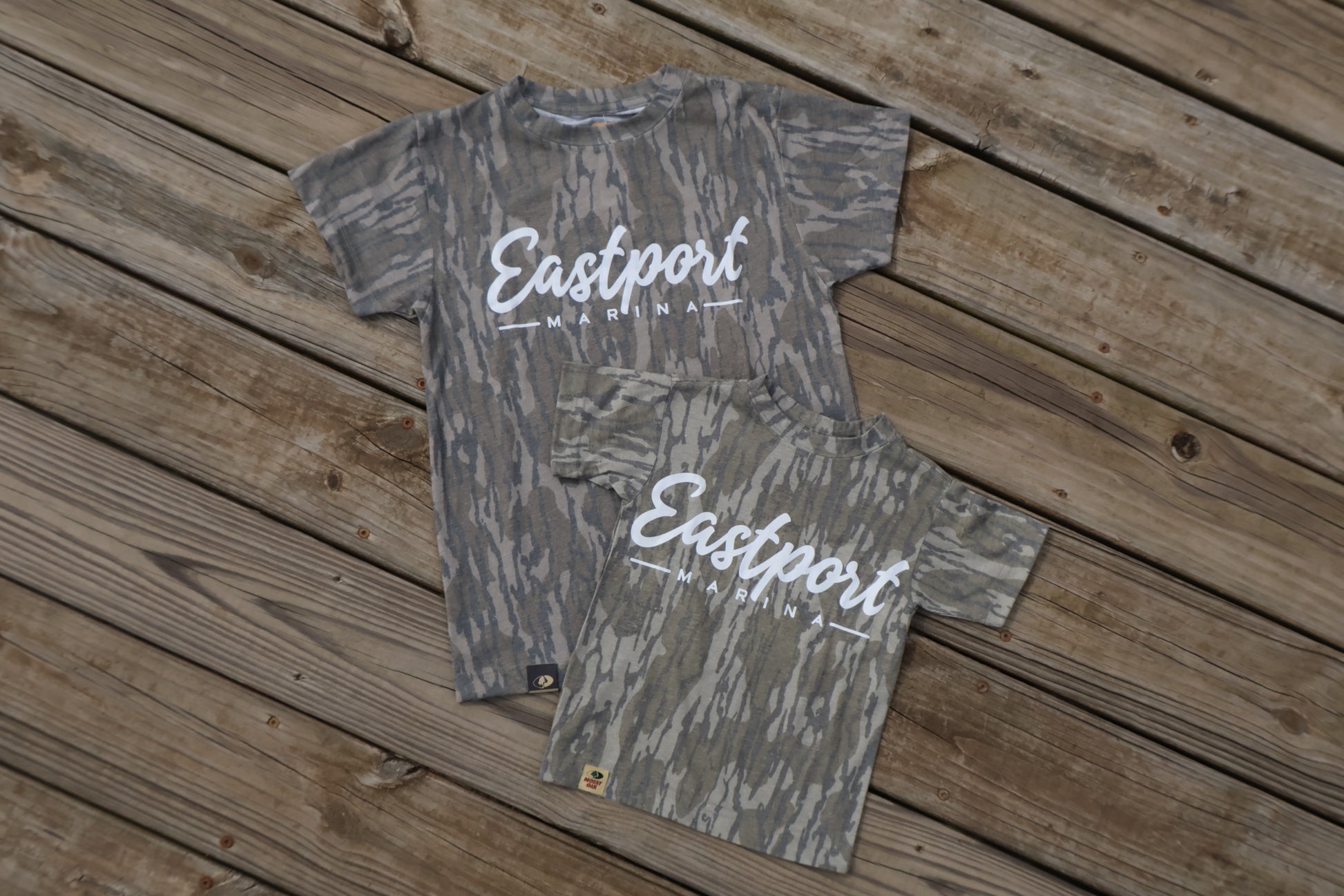 Two camouflage-patterned shirts with 'Eastport' branding on a wooden surface