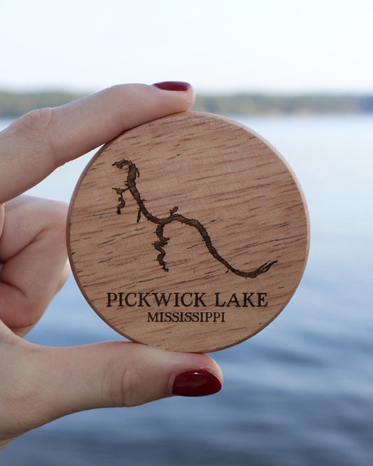 Hand holding a wooden magnetic bottle opener with 'Pickwick Lake, Mississippi' engraving against a lake background