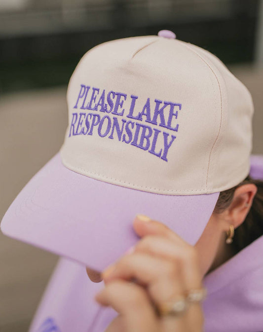 Beige cap with 'PLEASE LAKE RESPONSIBLY' text worn by a person in a purple hoodie.