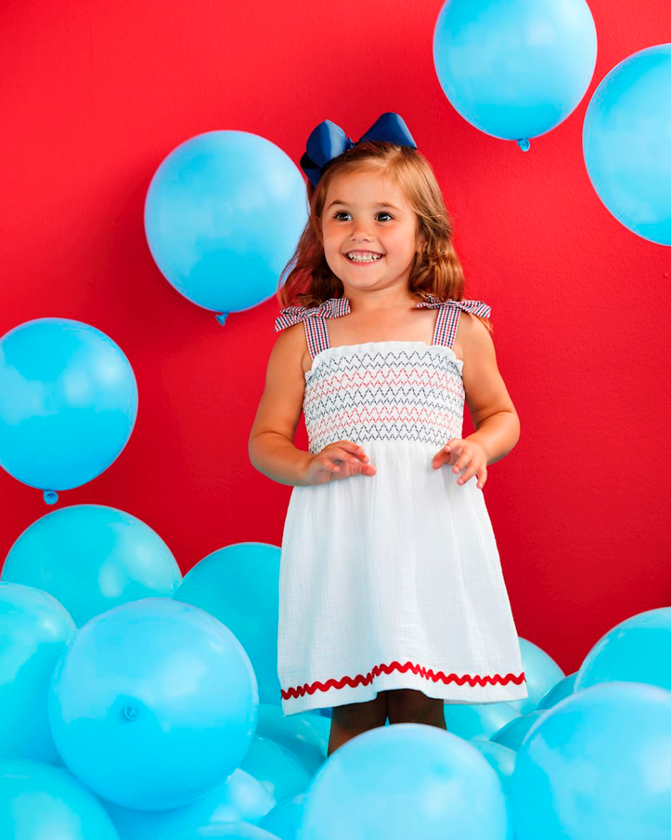 Young girl in a white dress with blue balloons against a red background