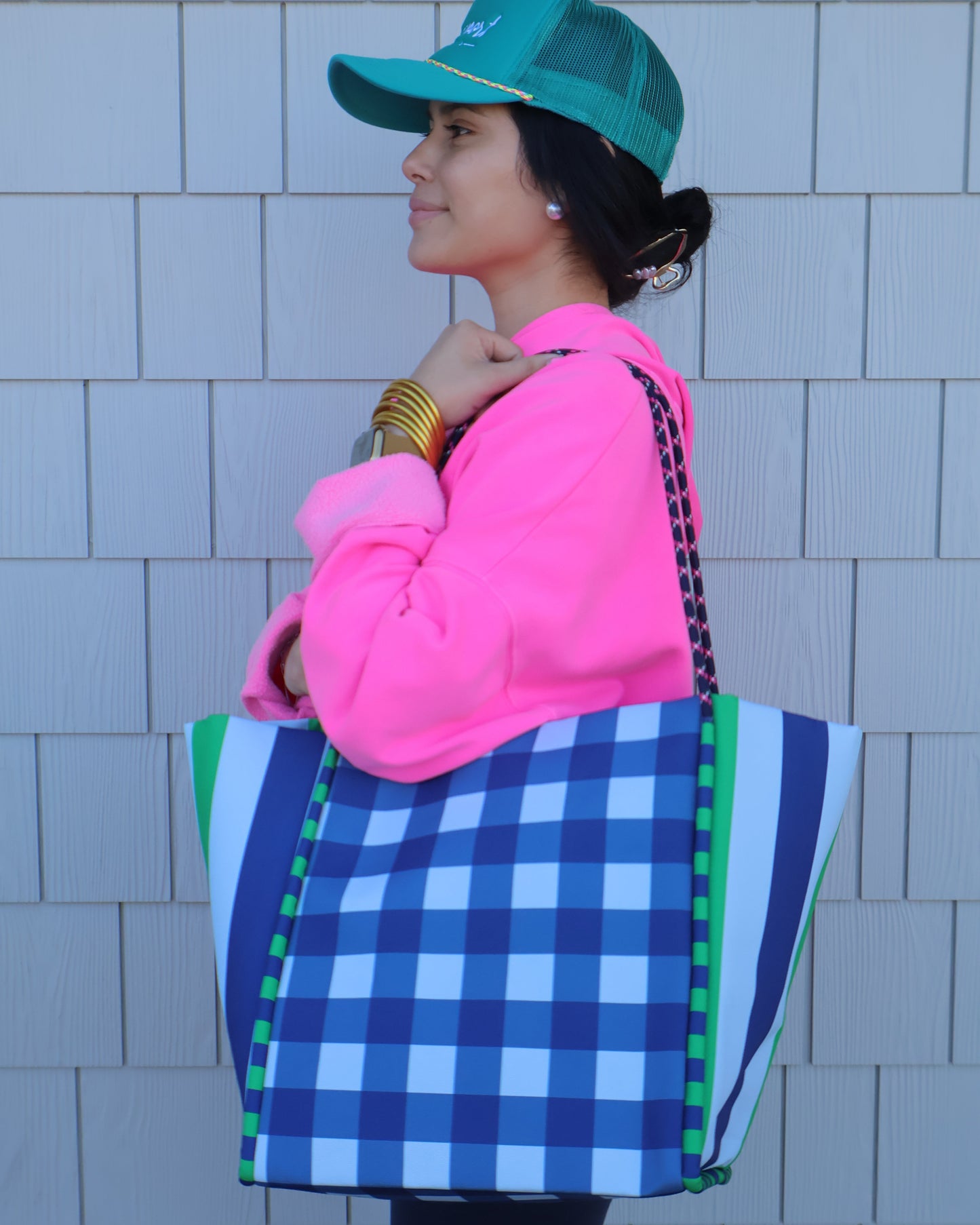 Person wearing a blue checkered bag, pink hoodie, and green hat on a tiled floor.