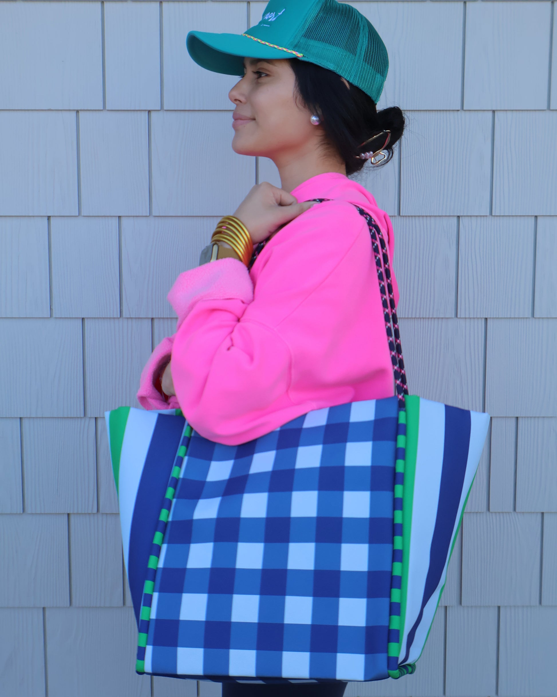 Person wearing a blue checkered bag, pink hoodie, and green hat on a tiled floor.