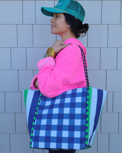 Person wearing a blue checkered bag, pink hoodie, and green hat on a tiled floor.