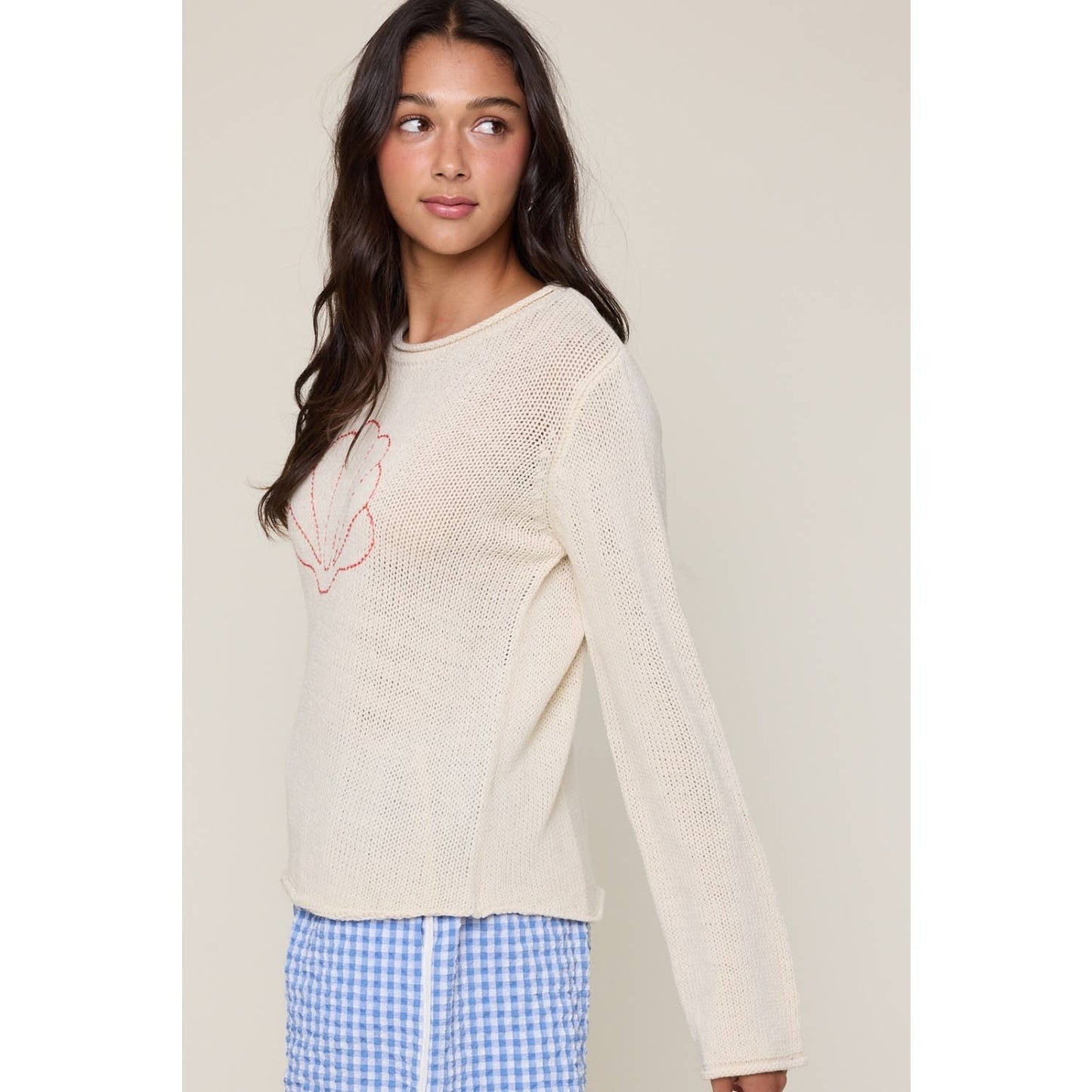 Woman wearing a cream sweater with a logo and blue checkered pants on a beige background