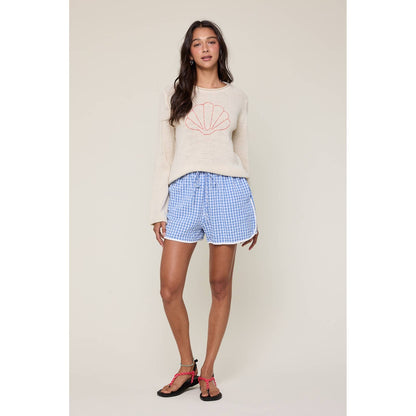 Woman wearing a beige sweater with a geometric design and blue checkered shorts on a plain background