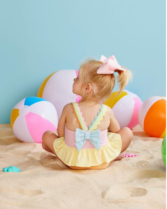 Child in a colorful swimsuit sitting on sand with beach balls in the background